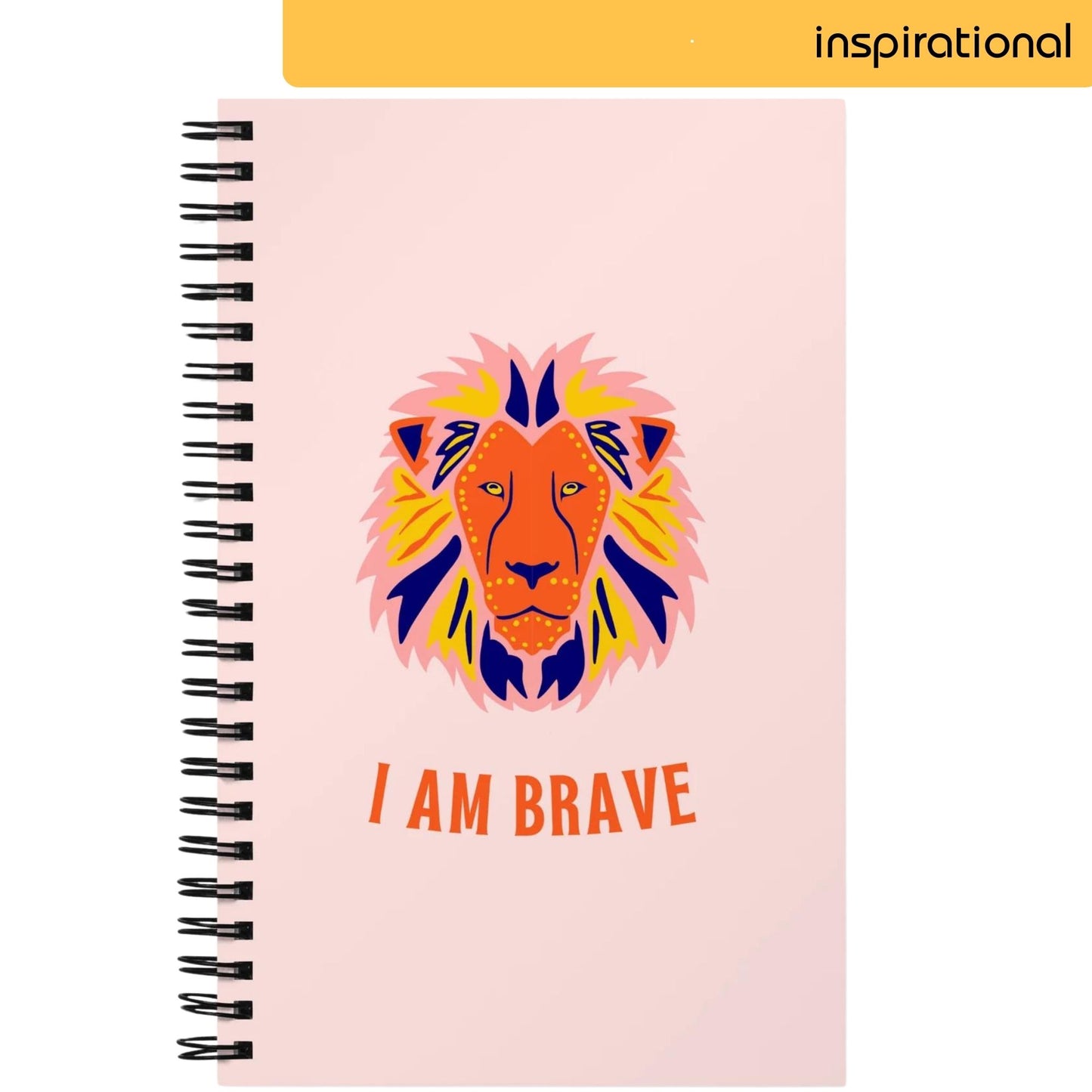 A notepad with a soft pink background features a vibrant, stylized illustration of a lion's face in bold colors, with the empowering statement 'I AM BRAVE' written beneath it, evoking a sense of courage and fearlessness.