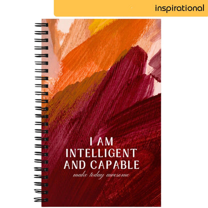 A notepad with a bold abstract background in strokes of red, orange, and yellow, features the confident affirmation 'I AM INTELLIGENT AND CAPABLE' in black letters, followed by the phrase 'make today awesome' in smaller text, conveying a message of self-empowerment and motivation.