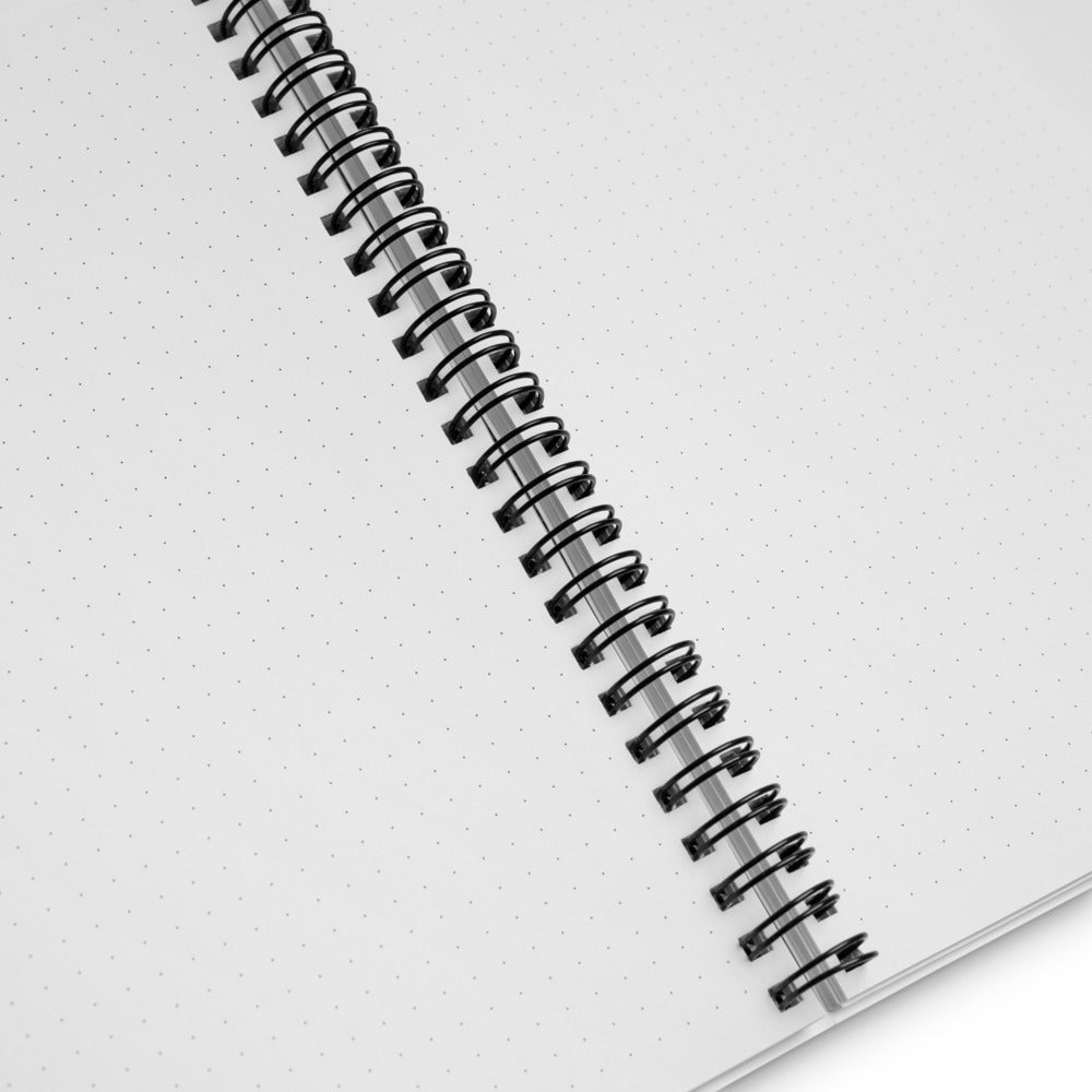 Close-up view of the black spiral binding of a dotted white notebook, showcasing the detail of the coil and the texture of the paper, on a clean, bright background.