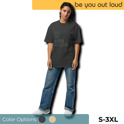 Woman modeling a faded black "All We Need Is Love" slogan oversized t-shirt by Be You Out Loud, available in sizes S to 3XL and color options shown in swatches.