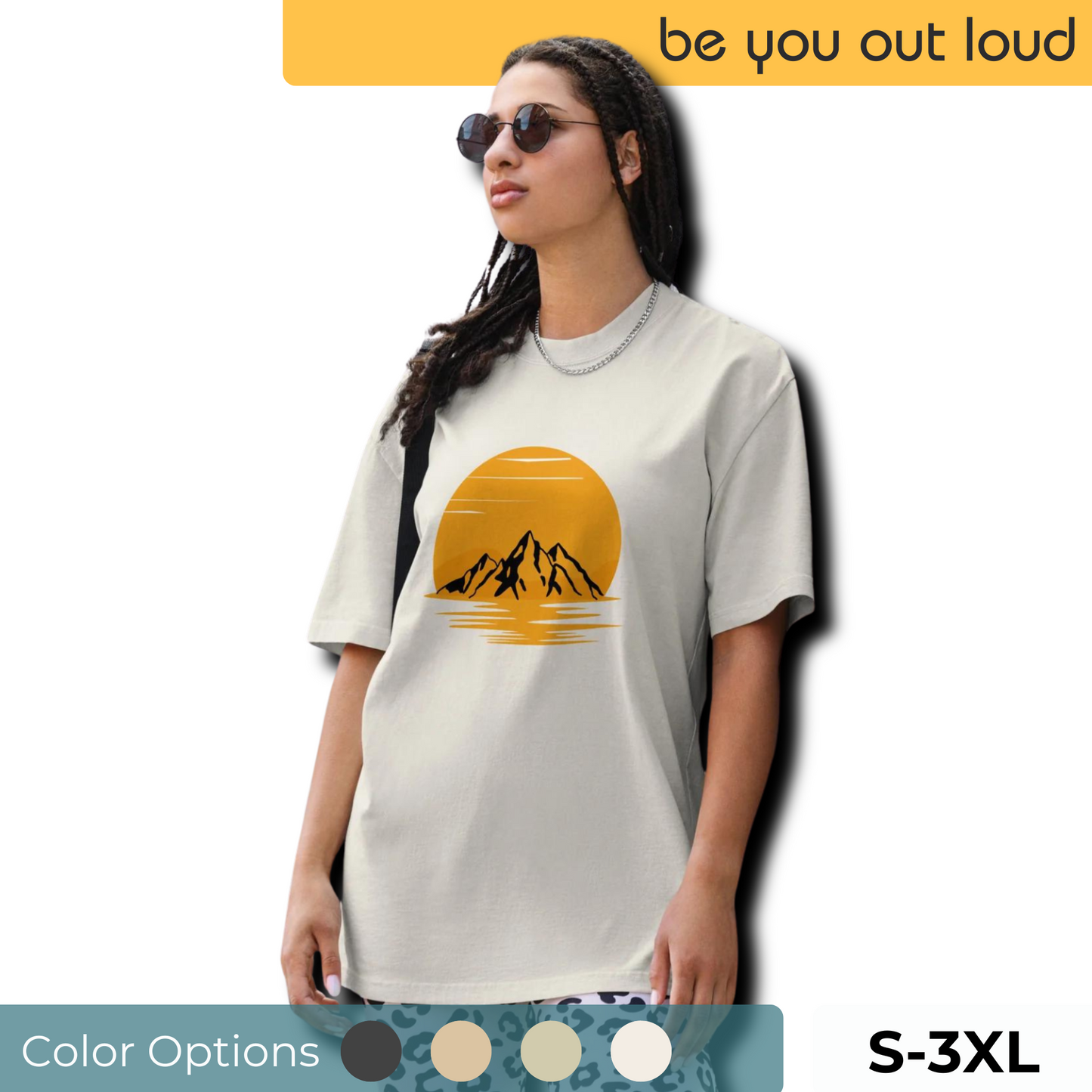 Stylish woman wearing Be You Out Loud's cream-colored 'Urban Adventure' oversized t-shirt featuring a bold sunset and mountain graphic, available in sizes S-3XL with color swatches displayed.