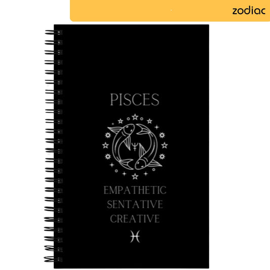 The notepad shows 'PISCES' in white letters on a black background, above an artistic line drawing of two fish forming a circle, a symbol for Pisces. Traits associated with this zodiac sign, 'EMPATHETIC SENSITIVE CREATIVE', are written underneath, with the astrological symbol for Pisces at the bottom.