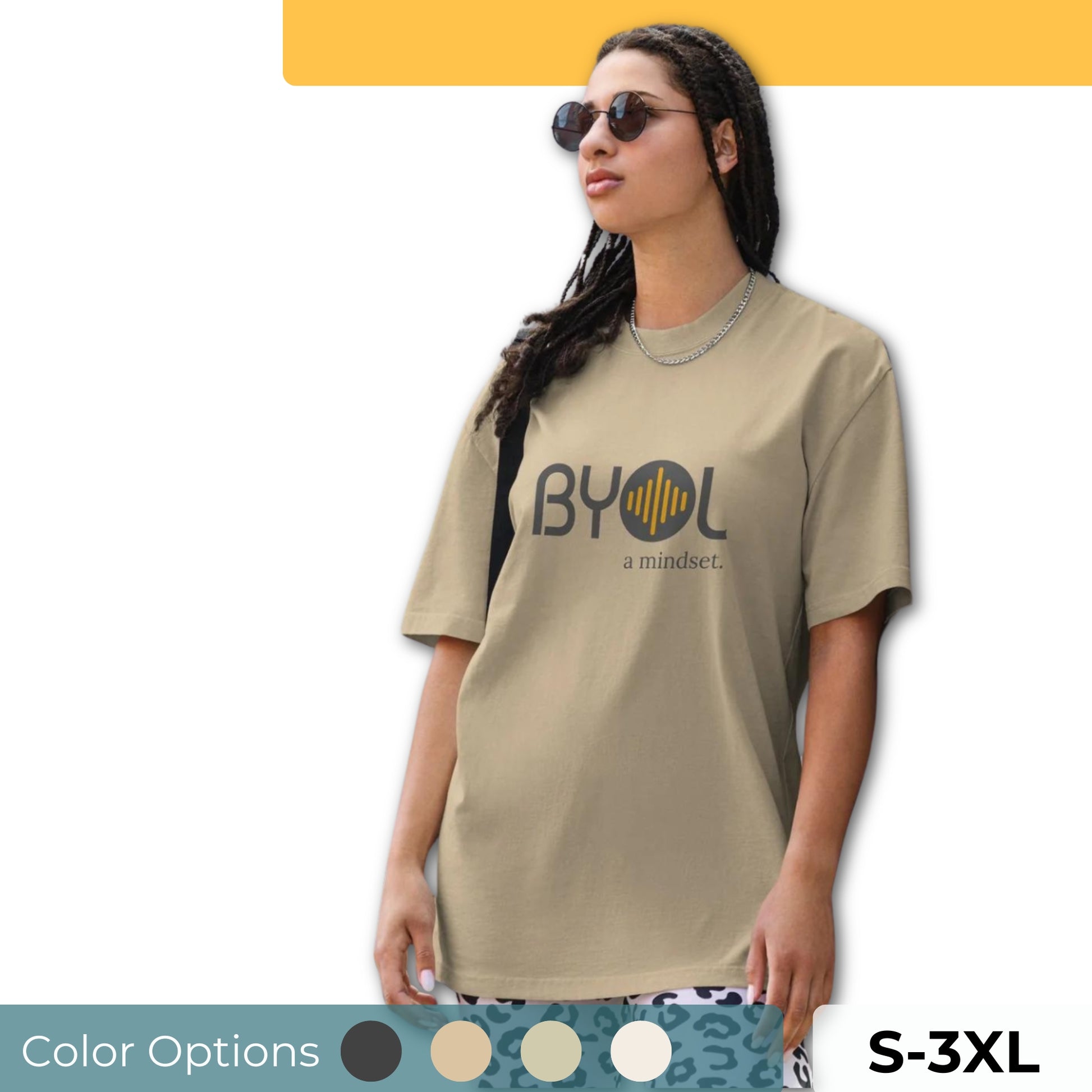 A young woman with long braids wearing sunglasses and a beige "BYOL: a mindset" T-shirt, standing and looking to the side. The T-shirt features the "BYOL" logo in dark gray and yellow on the front and is available in multiple colors (dark gray, beige, light blue, white, plus more) and sizes (S-3XL). The "be you out loud" logo is displayed at the top.