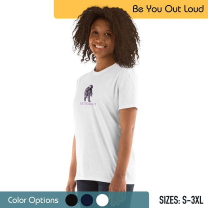 A woman with curly hair smiling and wearing a white T-shirt with a small illustration of an astronaut and the word "ASTRONAUT" below it. The background includes the slogan "Be You Out Loud," a color options palette, and available T-shirt sizes from S to 3XL.