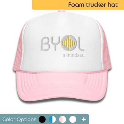 White and pink foam trucker hat with "BYOL a mindset" embroidered on the front in gray and yellow, displayed against a clean background. Available in various colors: black, white and blue, blue, pink, and white.