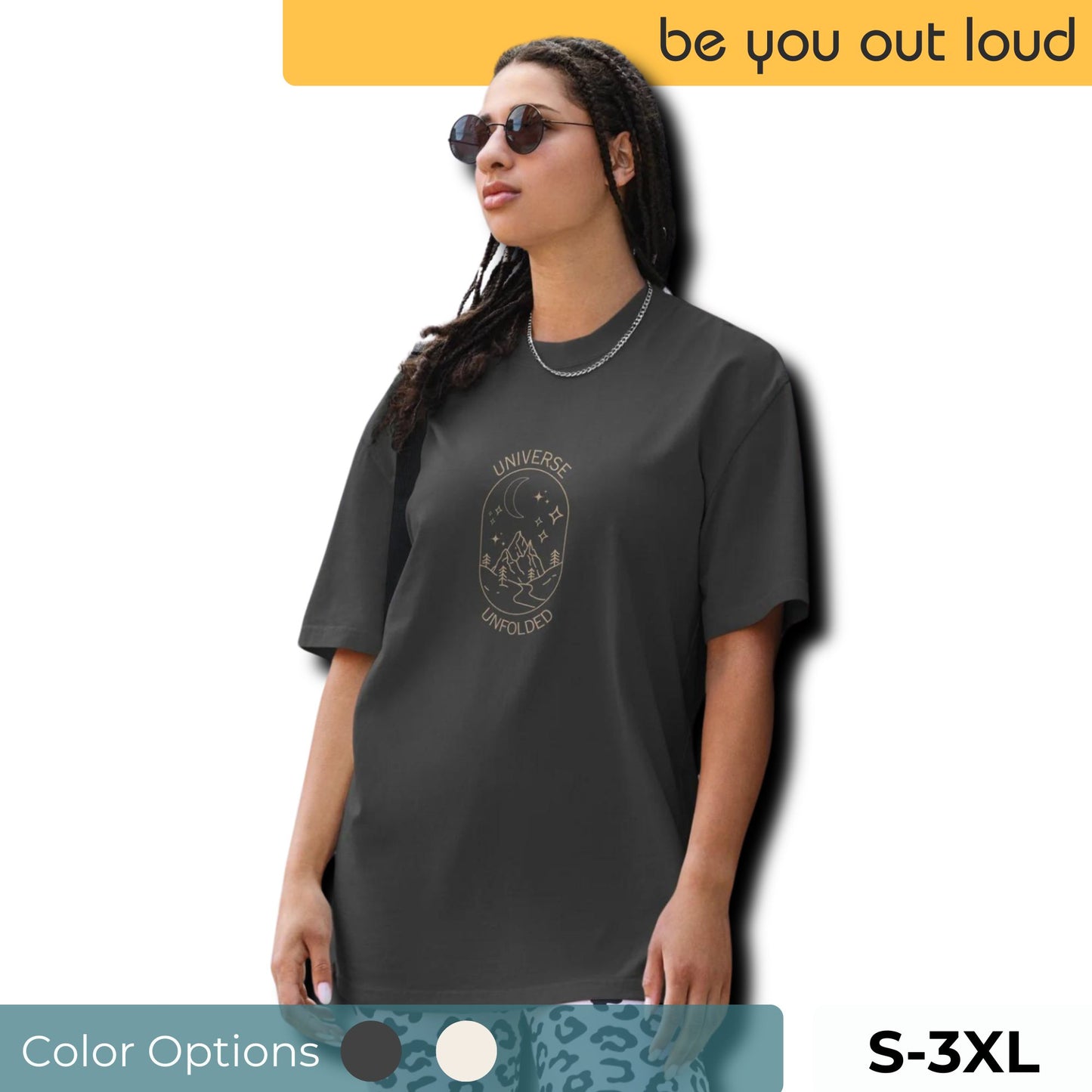 Trendsetting woman wearing a Be You Out Loud Oversized Tee in faded black, featuring a 'Universe Unfolded' graphic design that suggests cosmic exploration and self-discovery, accented with fashion-forward accessories. Showing the available sizes of 3-3xl and showing the two color options