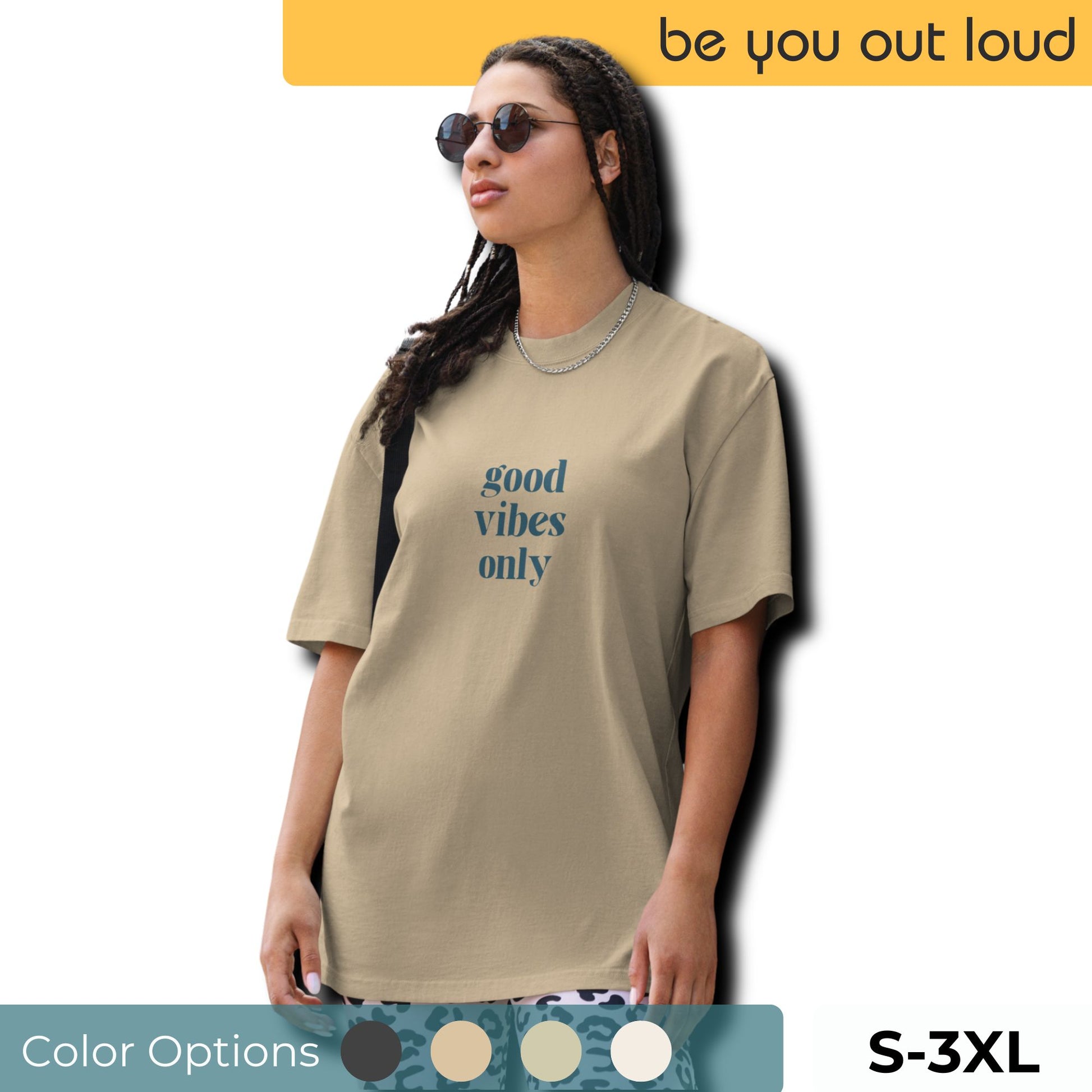 Fashion-savvy woman in Be You Out Loud's Good Vibes Only Oversized Tee, featuring a minimalist design that promotes a positive message, crafted in a chic taupe hue, complemented by stylish sunglasses and a silver necklace.