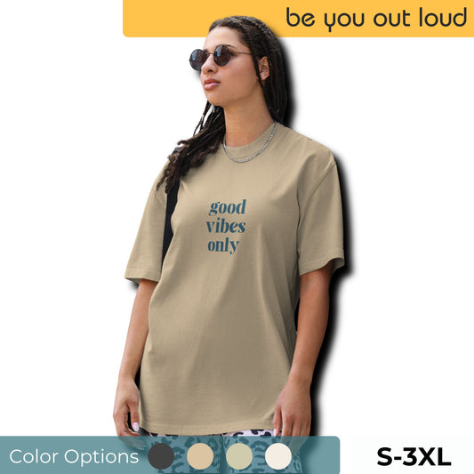 Fashion-savvy woman in Be You Out Loud's Good Vibes Only Oversized Tee, featuring a minimalist design that promotes a positive message, crafted in a chic taupe hue, complemented by stylish sunglasses and a silver necklace.