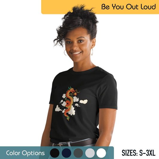 A woman with her hair styled up, wearing hoop earrings and a black T-shirt featuring a colorful design of a dragon among clouds. The background showcases the "Be You Out Loud" motto, a color options palette, and size availability from S to 3XL.