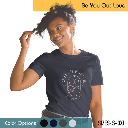 A woman with a playful hairstyle is wearing a dark blue T-shirt with a circular graphic that reads "UNIVERSE EVOLVED" with a mountain and river design inside the circle. She's standing against a background that includes the campaign phrase "Be You Out Loud," along with a color palette and size range from S to 3XL.