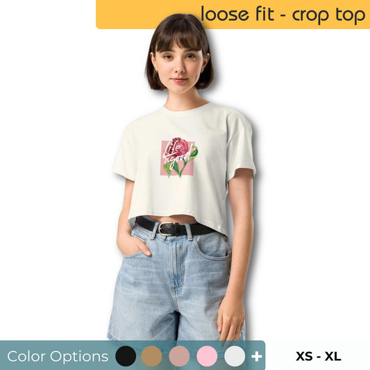 Woman wearing a loose-fit, off-white crop top with a playful 'life's good' rose design, paired with light-wash denim shorts showing an array of color options and sizes xs-xl