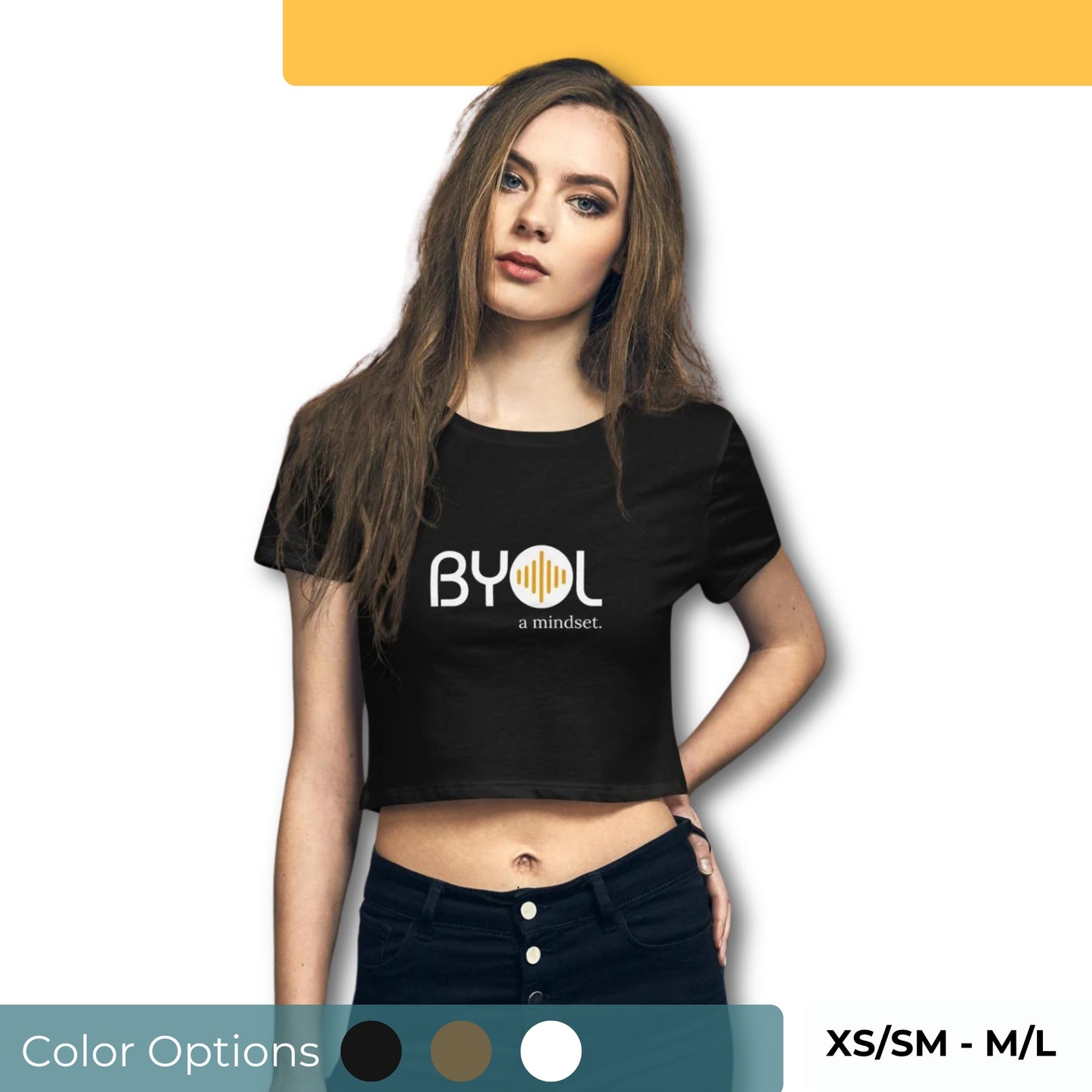 A young woman with long brown hair wearing a black "BYOL: a mindset" crop top, standing with one hand on her hip. The crop top features the "BYOL" logo in white and yellow on the front and is available in multiple colors (black, brown, white, light blue, plus more) and sizes (XS/SM - M/L). The "be you out loud" logo is displayed at the top.