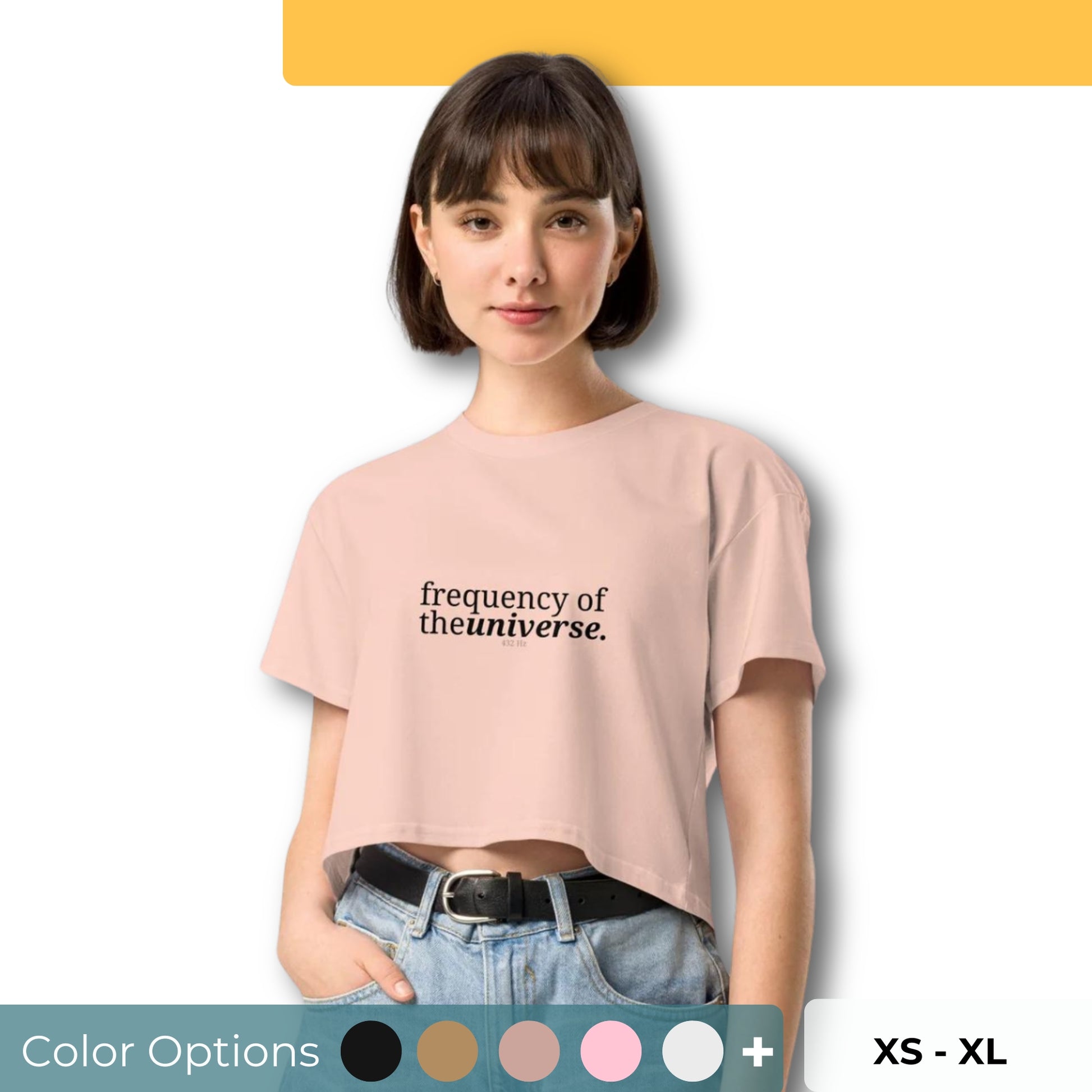 Woman wearing a pale pink cropped t-shirt with the phrase "frequency of the universe" printed in black, posing against a clean background. Available in various colors: black, brown, pink, green, and white. Sizes range from XS to XL.