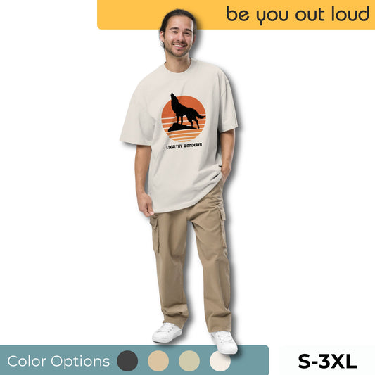 Smiling man wearing Be You Out Loud Men's "Stealthy Wanderer" Oversized Graphic Tee in a light beige color, featuring a bold fox silhouette against an orange backdrop, available in sizes S-3XL with various color options.