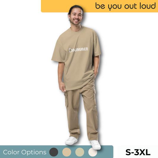 Cheerful man wearing the Be You Out Loud Men's "Rhythmic Soul" Oversized Graphic Tee in tan, featuring a minimalist drum set design, available in sizes S-3XL with a palette of color options.
