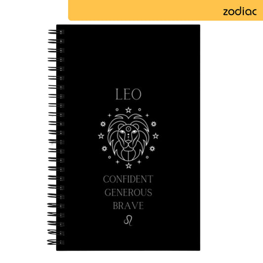 Black spiral notebook with Leo zodiac sign design, featuring a stylized white lion illustration surrounded by stars and text that reads 'Confident Generous Brave' in white, symbolizing astrological traits of the Leo sign.