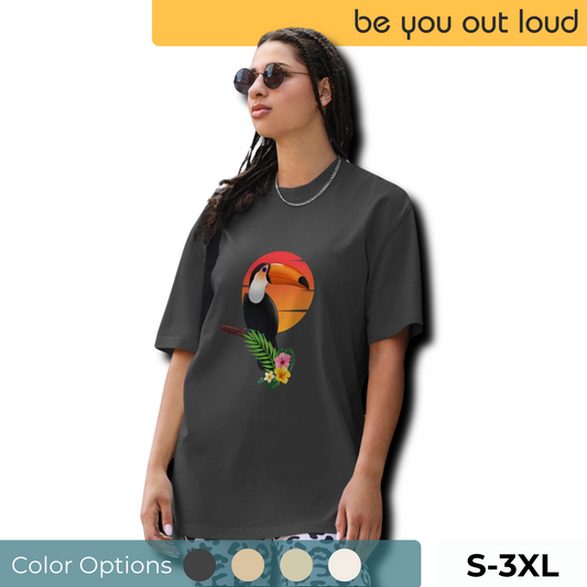 Woman wearing a dark grey oversized tee featuring a vivid toucan graphic with tropical foliage, promoting self-expression in sizes S to 3XL.