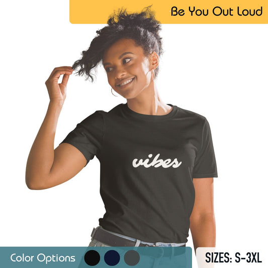 A woman with a playful hairstyle is wearing a black T-shirt with the word "vibes" in white cursive text. She's smiling and touching her hair, with a background that includes the "Be You Out Loud" message, a set of color options, and available T-shirt sizes from S to 3XL.