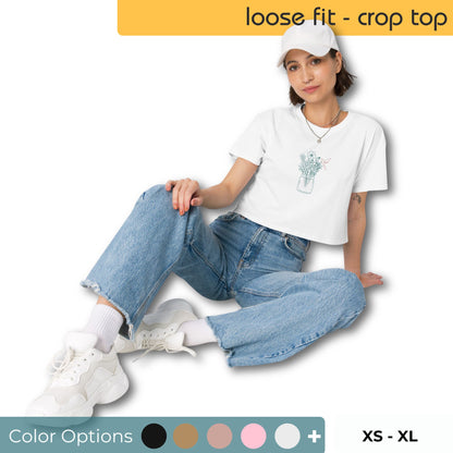 Woman wearing a loose-fit crop top with a delicate floral jar graphic design, representing comfortable and authentic fashion by BYOL. Also showing multiple color options and available in sizes sx-sl