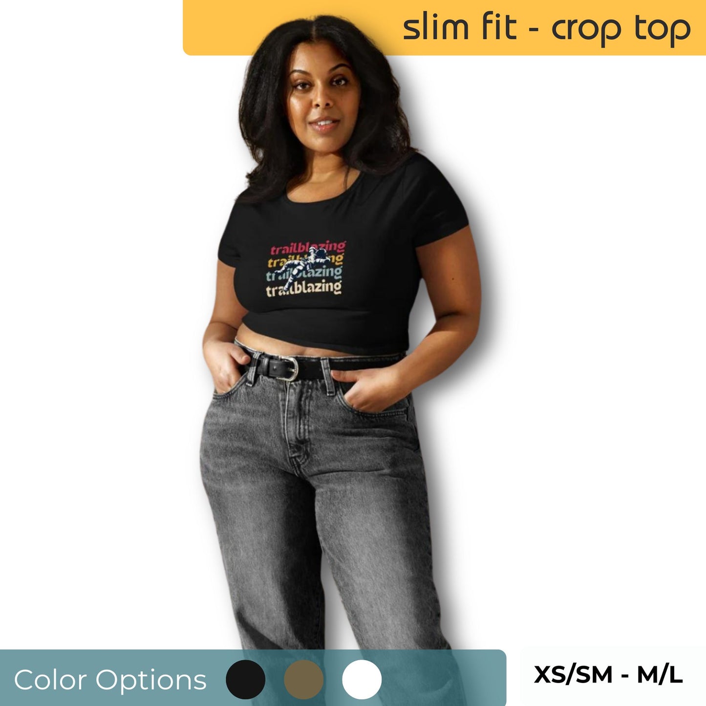 Woman wearing a slim-fit black crop top with colorful 'trailblazing' text, paired with high-waisted grey jeans, available in sizes XS/SM to M/L.