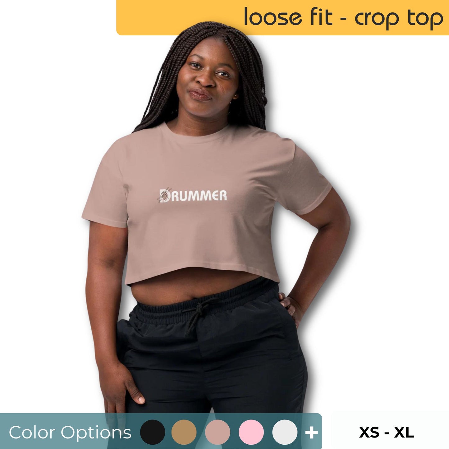 Woman posing in hazy pink loose-fit crop top with 'DRUMMER' printed in minimalist font, available in sizes XS through XL.