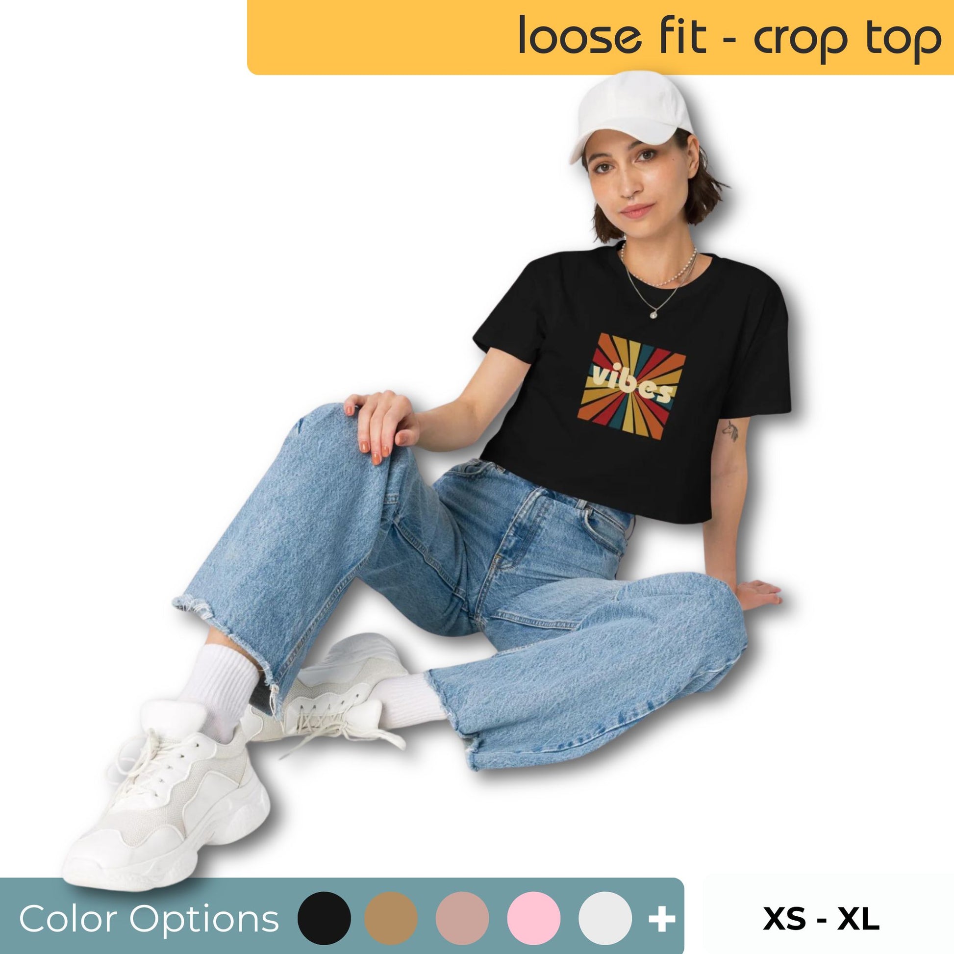 Relaxed woman in a black loose-fit crop top with a vibrant abstract design, complemented by baggy blue jeans and white sneakers, available in sizes XS to XL.