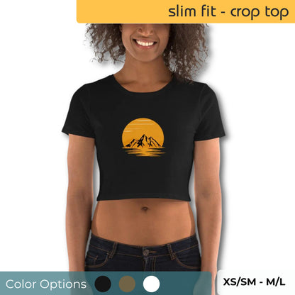 Smiling woman wearing a black slim-fit crop top with a golden sunset and mountain silhouette design, available in sizes XS/SM to M/L.