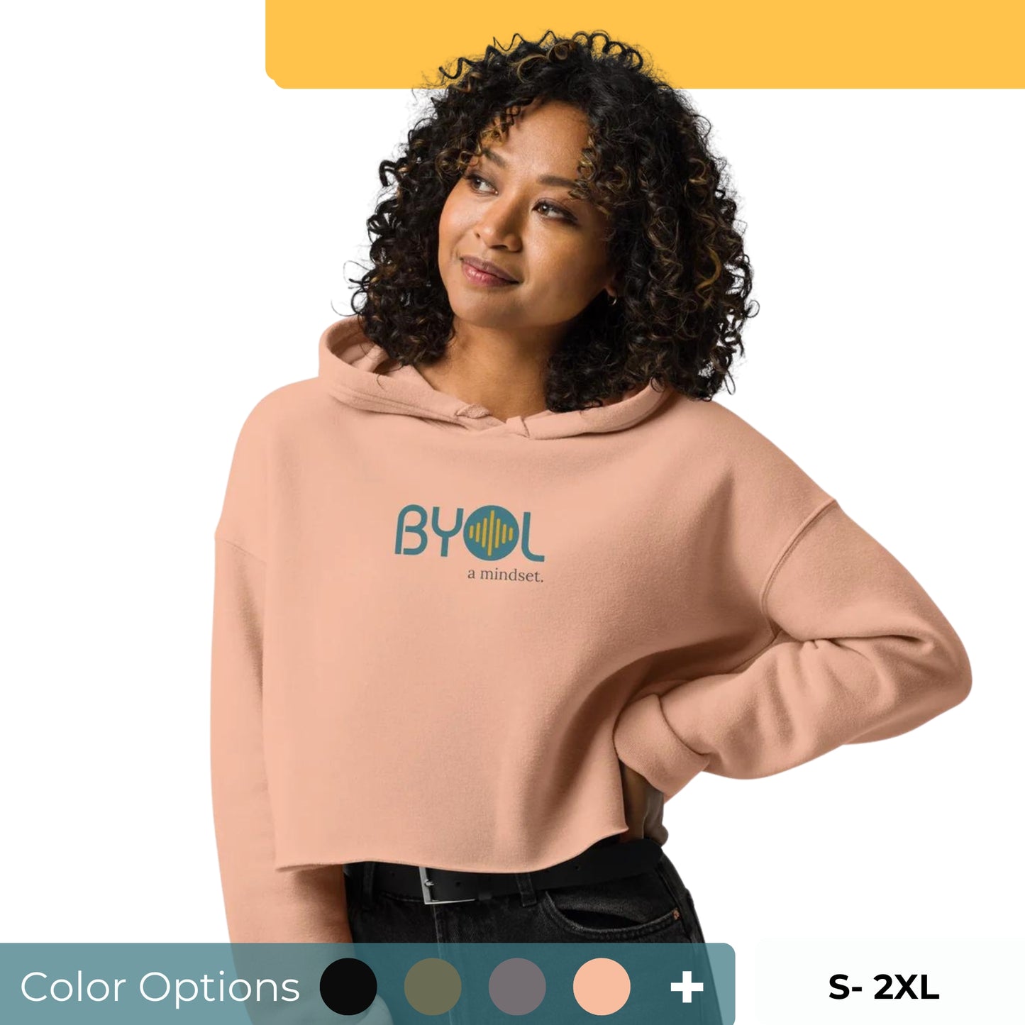 Woman wearing a cropped dusty pink BYOL mindset hoodie with color options in black, green, gray, and pink, available in sizes S to 2XL.