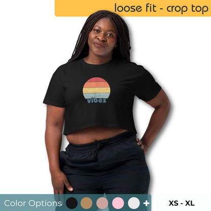 Woman smiling confidently in a black loose-fit crop top with a retro sunset design and the word "vibes," complete with color options and sizes XS to XL visible.