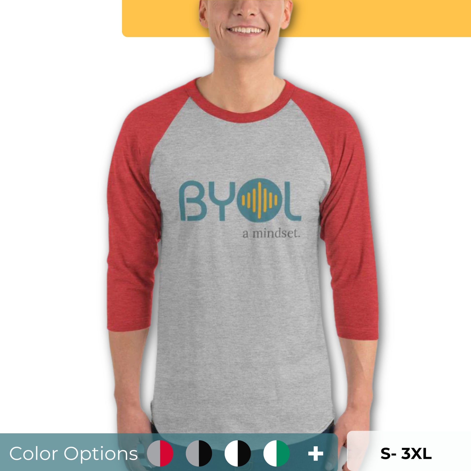 A young man wearing a gray and red "BYOL: a mindset" raglan T-shirt with three-quarter sleeves, smiling and standing with his arms at his sides. The T-shirt features the "BYOL" logo in teal and yellow on the front and is available in multiple colors (red, black, white, green, plus more) and sizes (S-3XL). The "be you out loud" logo is displayed at the top.