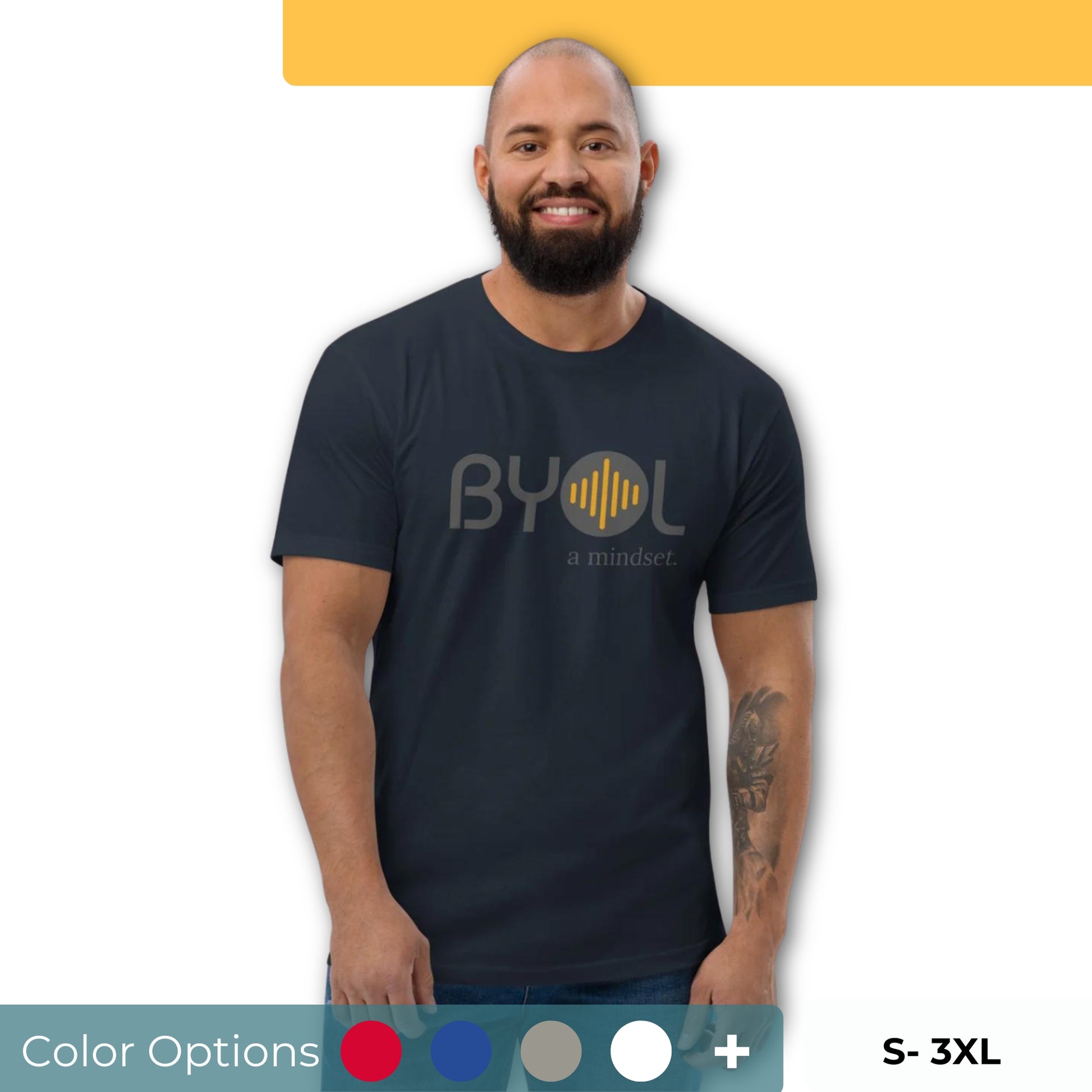 A bearded man with a shaved head wearing a navy blue "BYOL: a mindset" T-shirt, smiling and standing with his arms at his sides. The T-shirt features the "BYOL" logo in gray and yellow on the front and is available in multiple colors (red, blue, gray, white, plus more) and sizes (S-3XL). The "be you out loud" logo is displayed at the top.