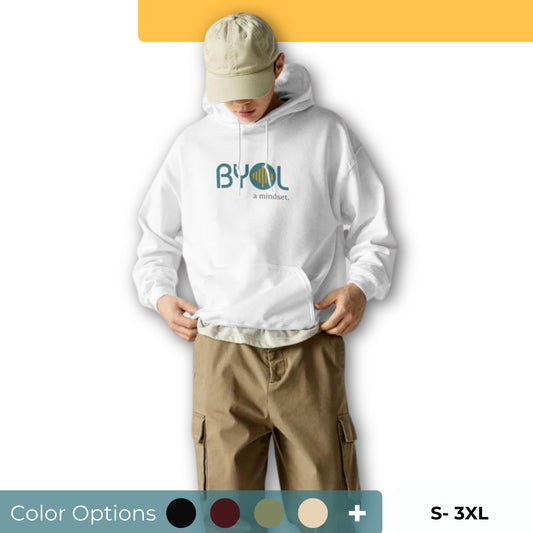 A young man wearing a white "BYOL: a mindset" hoodie, adjusting the hem and looking down. He is also wearing a beige cap and khaki pants. The hoodie features the "BYOL" logo in teal and yellow on the front and is available in multiple colors (black, maroon, green, beige, plus more) and sizes (S-3XL). The "be you out loud" logo is displayed at the top.