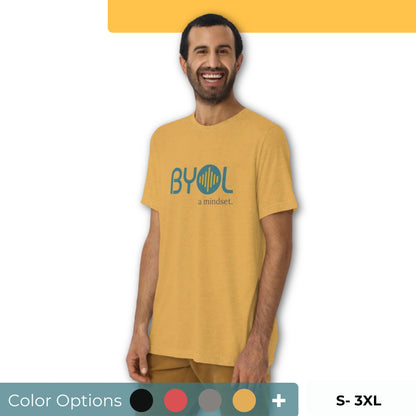 A young man with short dark hair and a beard wearing a yellow "BYOL: a mindset" T-shirt, smiling and standing with his arms at his sides. The T-shirt features the "BYOL" logo in teal and is available in multiple colors (black, red, gray, pink, yellow, plus more) and sizes (S-3XL). The "be you out loud" logo is displayed at the top.