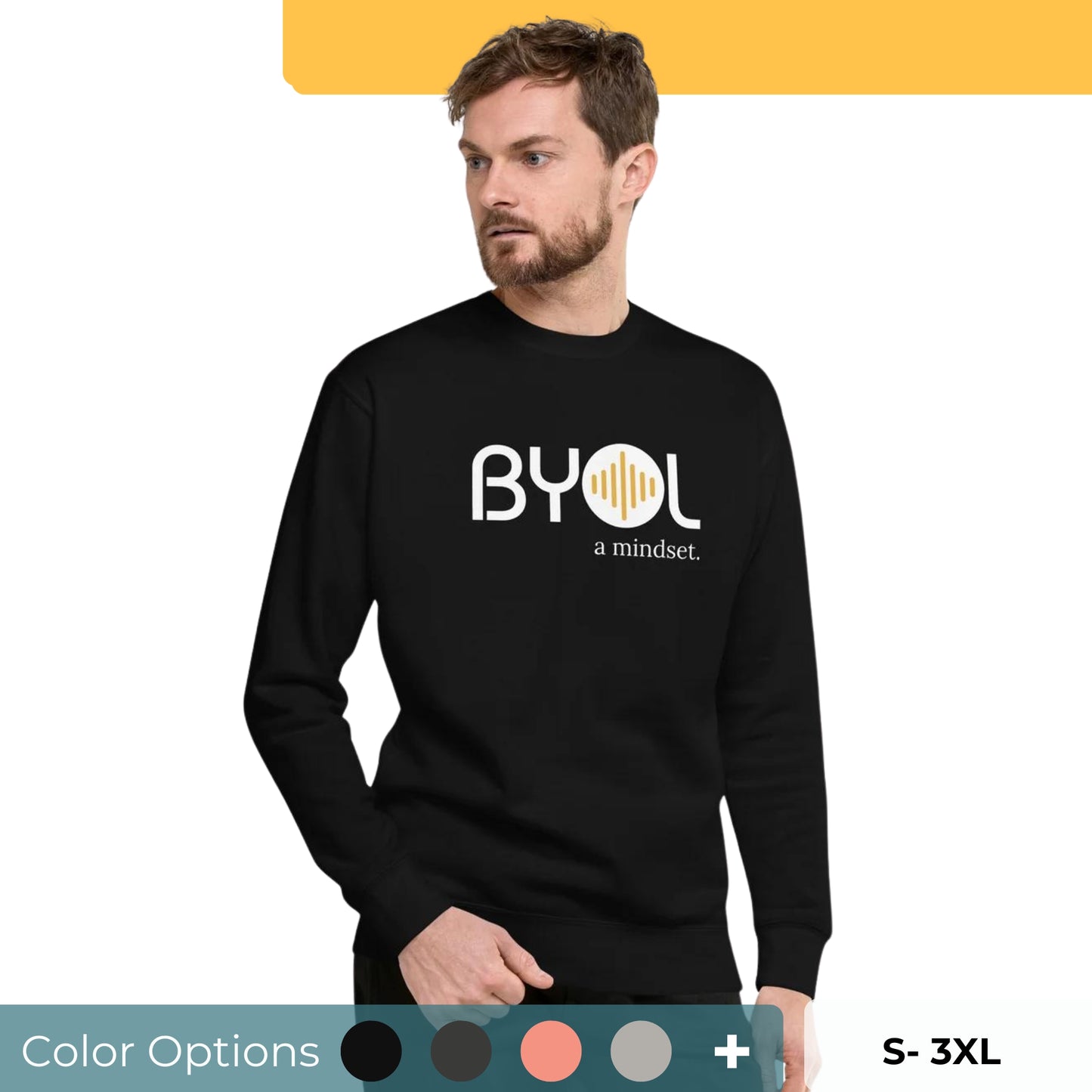 A young man with short hair and a beard wearing a black "BYOL: a mindset" sweatshirt, standing and looking to the side. The sweatshirt features the "BYOL" logo in white and yellow on the front and is available in multiple colors (black, dark gray, light gray, pink, plus more) and sizes (S-3XL). The "be you out loud" logo is displayed at the top.