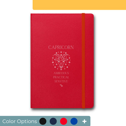 Red notebook with elastic closure featuring a Capricorn zodiac sign design in white, depicting a stylized goat's head with stars and text that reads 'Ambitious, Practical, Sensitive' for Capricorn traits.