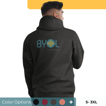 A young man wearing a dark gray "BYOL: a mindset" hoodie, viewed from the back. The hoodie features the "BYOL" logo in teal and yellow on the back and is available in multiple colors (black, red, maroon, brown, plus more) and sizes (S-3XL). The "be you out loud" logo is displayed at the top.