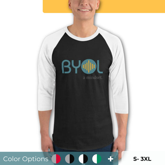 A young man wearing a black and white "BYOL: a mindset" raglan T-shirt with three-quarter sleeves, smiling and standing with his arms at his sides. The T-shirt features the "BYOL" logo in teal and yellow on the front and is available in multiple colors (red, black, white, green, plus more) and sizes (S-3XL). The "be you out loud" logo is displayed at the top.