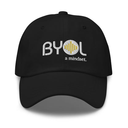 Black classic dad hat with "BYOL a mindset" embroidered on the front in white and yellow, displayed against a clean background. Available in various colors: black, gray, green, pink, and tan.