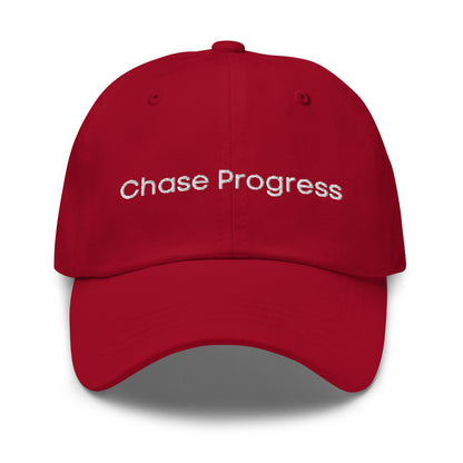 A red dad hat with the phrase "Chase Progress" embroidered in white stitching across the front.