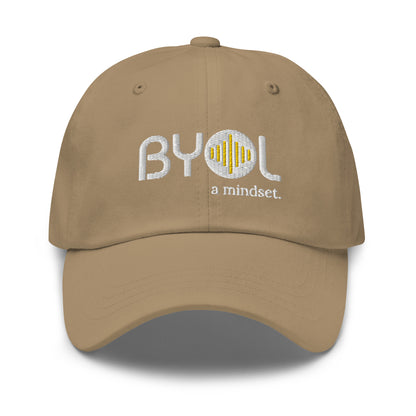 Khaki classic dad hat with "BYOL a mindset" embroidered on the front in white and yellow, displayed against a clean background. Available in various colors: black, gray, green, pink, and tan.