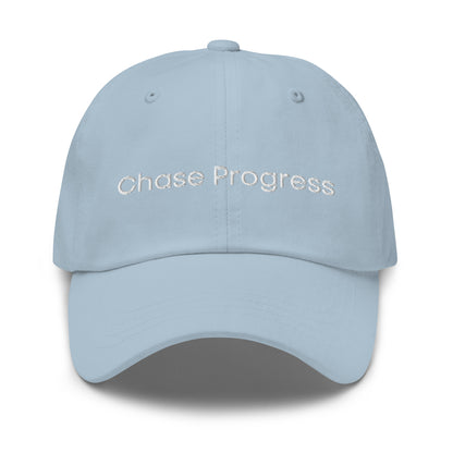 A light blue dad hat with the phrase "Chase Progress" embroidered in white stitching across the front.