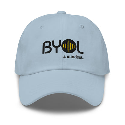 Light blue classic dad hat with "BYOL a mindset" embroidered on the front in black and yellow, displayed against a clean background. Available in various colors: black, gray, green, pink, and white.