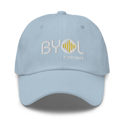 Light blue classic dad hat with "BYOL a mindset" embroidered on the front in white and yellow, displayed against a clean background. Available in various colors: black, gray, green, pink, and tan.