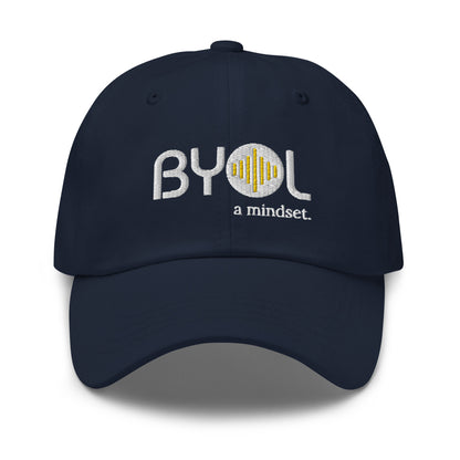 Navy blue classic dad hat with "BYOL a mindset" embroidered on the front in white and yellow, displayed against a clean background. Available in various colors: black, gray, green, pink, and tan.