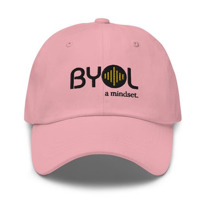 Pink classic dad hat with "BYOL a mindset" embroidered on the front in black and yellow, displayed against a clean background. Available in various colors: black, gray, green, pink, and white.