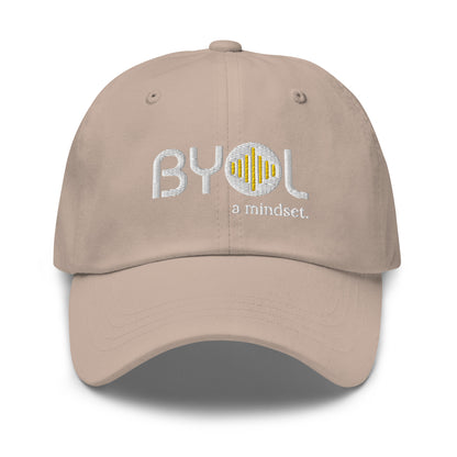 Tan classic dad hat with "BYOL a mindset" embroidered on the front in white and yellow, displayed against a clean background. Available in various colors: black, gray, green, pink, and tan.