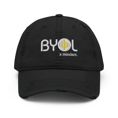 Black distressed dad hat with "BYOL a mindset" embroidered on the front in white and yellow, displayed against a clean background. Available in various colors: black, navy blue, gray, green, and beige.