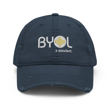 Navy blue distressed dad hat with "BYOL a mindset" embroidered on the front in white and yellow, displayed against a clean background. Available in various colors: black, navy blue, gray, green, and beige.