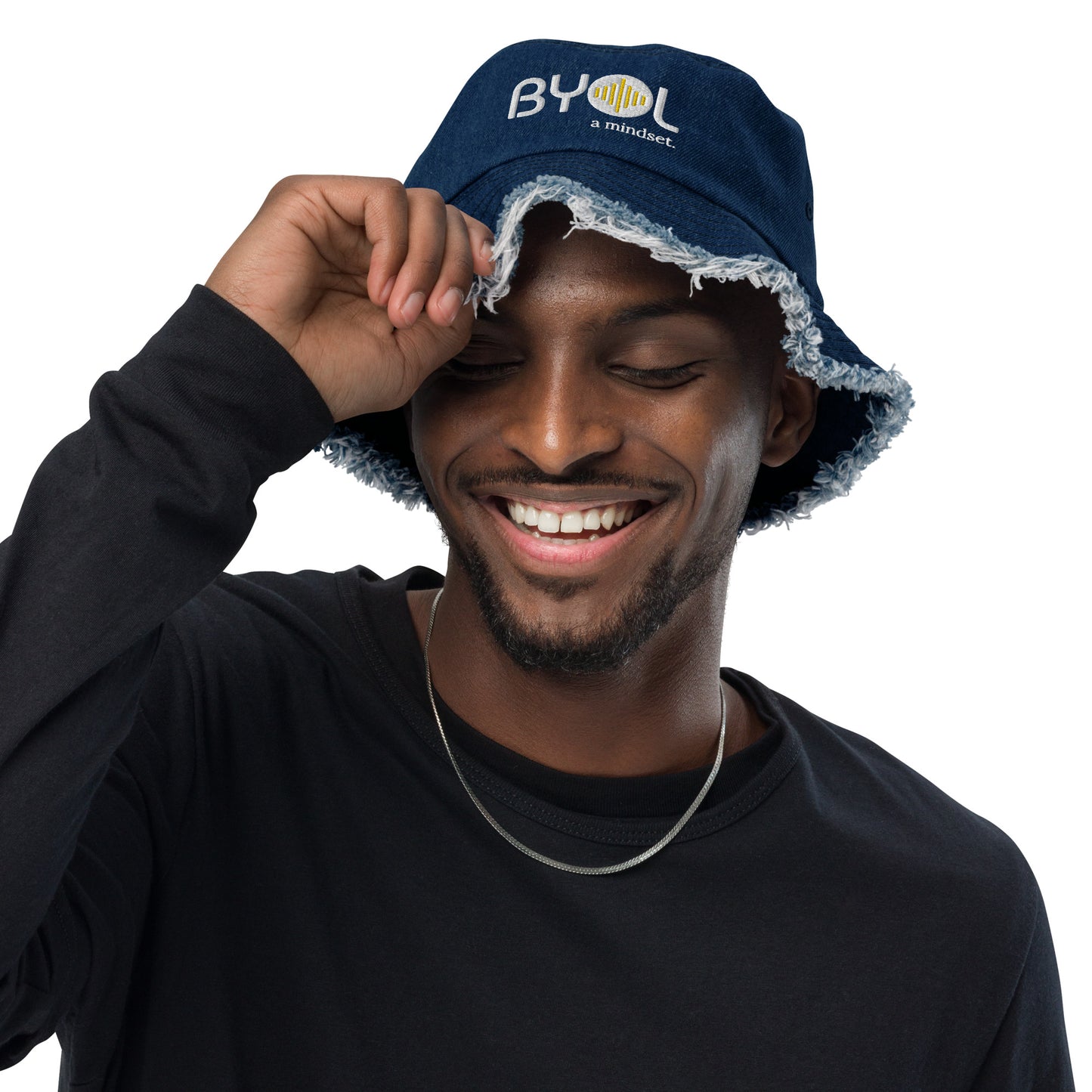 Man wearing a classic denim bucket hat with frayed edges and "BYOL a mindset" embroidered on the front in white and yellow, smiling and posing against a clean background. Available in various colors: black, dark blue, light blue, and teal.