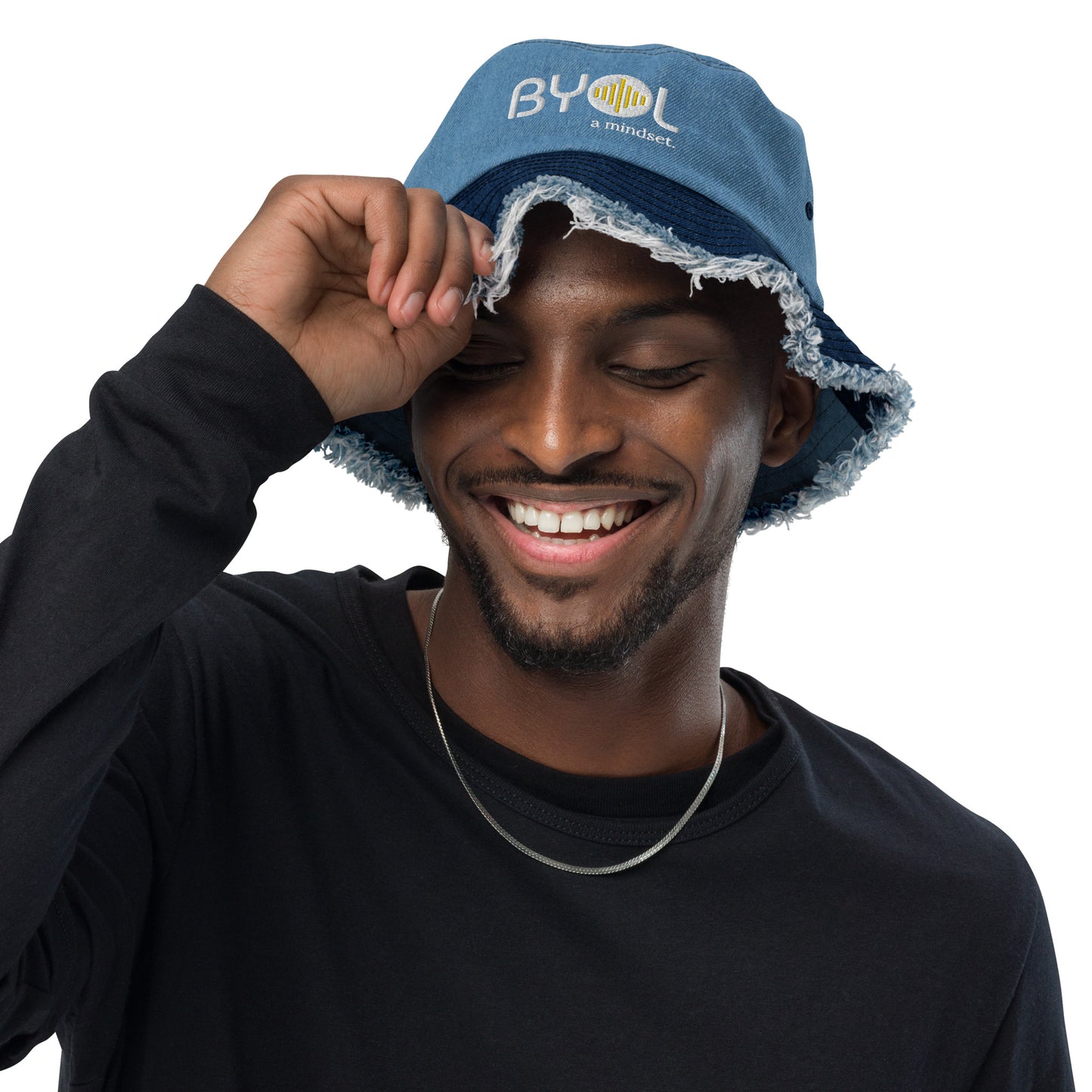 Man wearing a classic/light denim bucket hat with frayed edges and "BYOL a mindset" embroidered on the front in white and yellow, smiling and posing against a clean background. Available in various colors: black, dark blue, light blue, and teal.